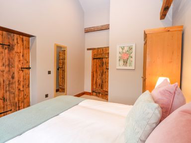 A bedroom with a bed with pillows and blanket a wooden wardrobe a wall mirror wooden doors and a framed picture at Shorthorn Barn in Attlebridge near Taverham
