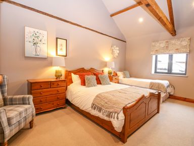 A bedroom with wooden bed frames two beds bedside tables lamps an armchair and a window at Shorthorn Barn in Attlebridge near Taverham