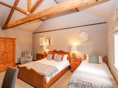 A bedroom with wooden beds a wooden wardrobe a plaid armchair and bedside tables at Shorthorn Barn Attlebridge near Taverham