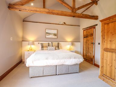A bedroom with a double bed and pillows two bedside tables with lamps wooden doors and exposed wooden ceiling beams at Shorthorn Barn in Attlebridge near Taverham