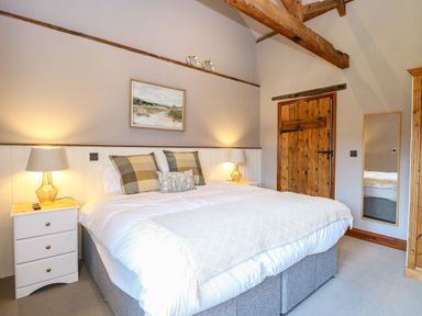 A bedroom with a large bed pillows bedside tables lamps a wooden door and a mirror at Shorthorn Barn in Attlebridge near Taverham
