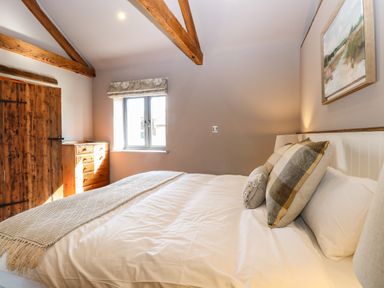 A bedroom with a bed pillows a wooden dresser window and wooden door at Shorthorn Barn in Attlebridge near Taverham