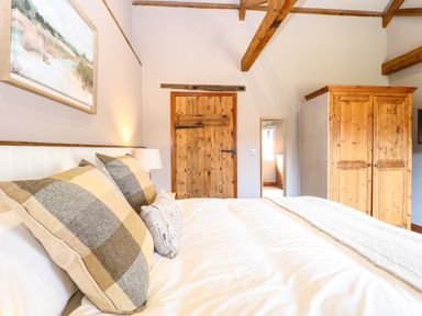 A bedroom with a bed with pillows a wooden door a mirror and a wooden wardrobe at Shorthorn Barn in Attlebridge near Taverham