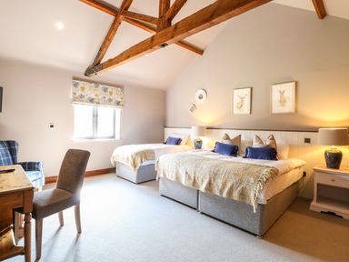 A bedroom with two beds bedside tables lamps a wooden desk and chair under wooden beams at Shorthorn Barn Attlebridge near Taverham