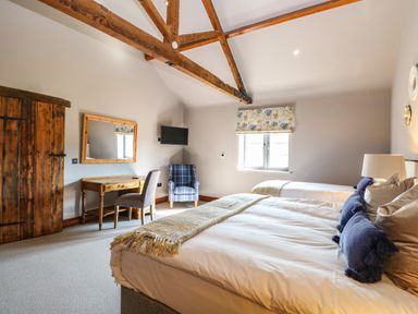 A bedroom with wooden beams a large bed a blue plaid armchair a wooden desk and a mirror at Shorthorn Barn Attlebridge near Taverham