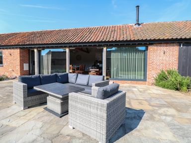 An outdoor patio with gray wicker seating and a table in front of a brick building with large windows at Shorthorn Barn in Attlebridge near Taverham