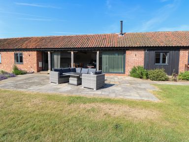 A patio area with outdoor seating on a paved surface in front of a single-story brick building at Shorthorn Barn in Attlebridge near Taverham