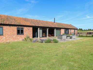 A single-story brick building with a tiled roof and outdoor seating on a patio surrounded by grass at Shorthorn Barn in Attlebridge near Taverham