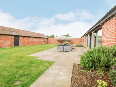 An outdoor patio with seating and umbrella between two red brick buildings at Shorthorn Barn in Attlebridge near Taverham