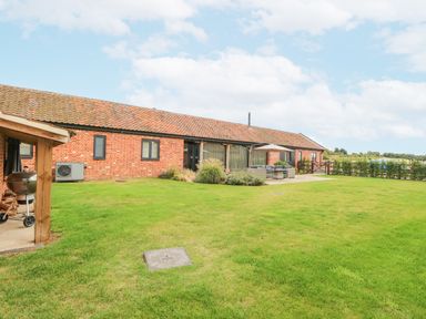 A lawn with patio furniture and a barbecue near a brick building at Shorthorn Barn in Attlebridge near Taverham