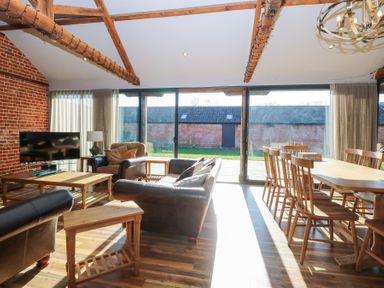 A living room with leather sofas a wooden dining table with chairs wooden beams and a brick wall at Shorthorn Barn in Attlebridge near Taverham