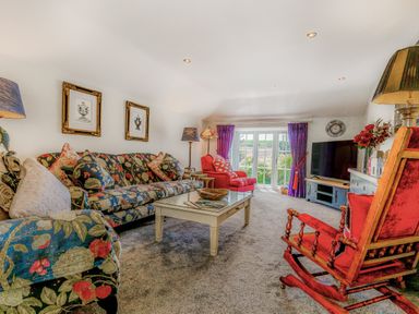 A living room with floral sofas red armchairs a coffee table and a television at Armando in Devoran Cornwall