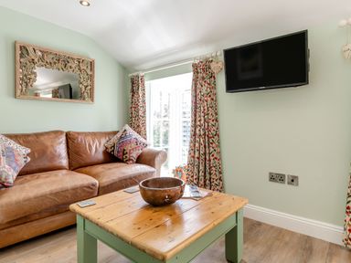 A living room with a brown leather sofa a wooden coffee table a wall mounted tv and patterned curtains at Armando in Devoran Cornwall