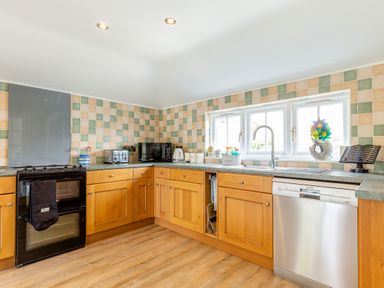 A kitchen with wooden cabinets a black oven a stainless steel dishwasher and square tiled walls at Armando in Devoran Cornwall