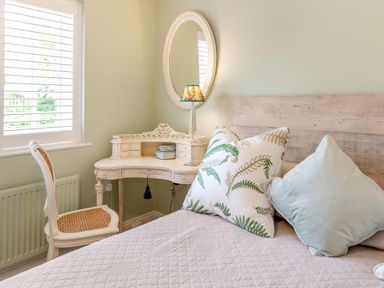 A bedroom with a wooden bed headboard pillows vintage white desk chair and oval mirror at Armando in Devoran Cornwall
