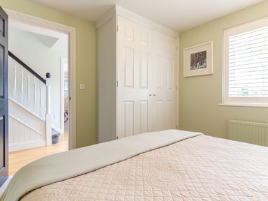 A bedroom with a bed covered in a quilt near a window with blinds a framed picture on the wall and a white built-in wardrobe at Armando in Devoran Cornwall