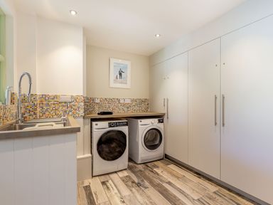 A laundry room with a washing machine dryer large cabinets mosaic tile backsplash and a sink at Armando in Devoran Cornwall