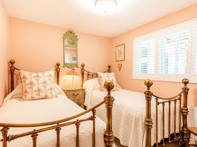 A bedroom with two brass beds a nightstand with a lamp a wall mirror and a window with shutters at Armando in Devoran Cornwall