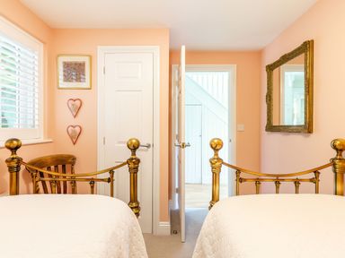 A bedroom with two brass beds a wooden chair a white door two heart decorations and a mirror on peach walls at Armando in Devoran Cornwall