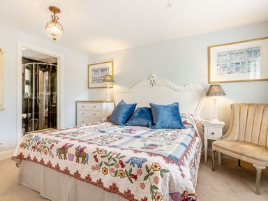 A bedroom with a large bed with a colorful quilt and blue pillows next to a dresser and a chair at Armando in Devoran Cornwall