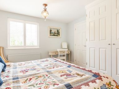 A bedroom with a bed covered with a patterned quilt a window with shutters a dresser with a mirror and white closets at Armando in Devoran Cornwall
