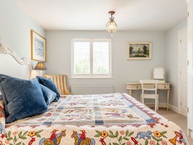 A bedroom with a bed covered with a quilt and blue pillows next to a chair and a dressing table under a window at Armando in Devoran Cornwall
