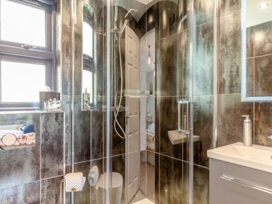A bathroom with a glass shower enclosure a sink with a soap dispenser and a window at Armando in Devoran Cornwall