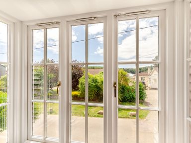 A view through large glass doors showing a garden with bushes and houses beyond at Armando in Devoran Cornwall