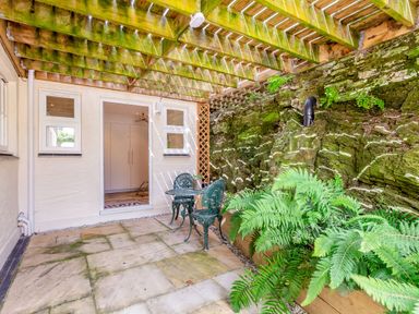 A small outdoor patio area with a glass table and two chairs under a wooden pergola at Armando in Devoran Cornwall