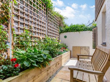 An outdoor patio area with a wooden bench a raised wooden planter with flowers and climbing plants on trellis at Armando in Devoran Cornwall