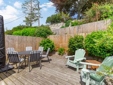 An outdoor wooden deck with a round table and six striped chairs and two green cushioned armchairs with a small wooden side table at Armando in Devoran Cornwall