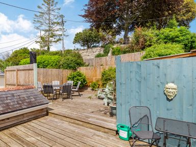 An outdoor wooden deck with patio chairs and table surrounded by wooden fences and greenery at Armando in Devoran Cornwall