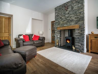 A living room with a stone fireplace leather sofas red cushions and a white rug at Fellside Lodge in Bowness-On-Windermere