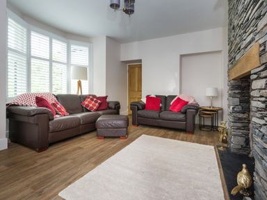 A living room with two brown leather sofas red cushions a stone fireplace and wooden floor at Fellside Lodge in Bowness-On-Windermere