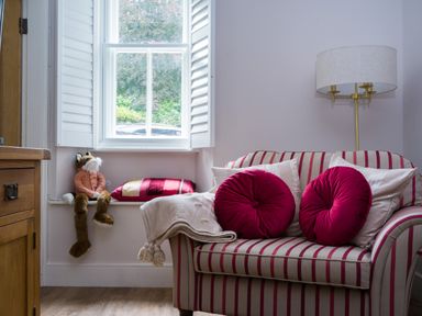 A sitting area with a striped armchair with red and white pillows next to a window with a stuffed animal and a cushion on the windowsill at Fellside Lodge in Bowness-On-Windermere