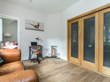 A room with a brown leather sofa wooden desk and stool sliding wooden doors and a doorway to another room