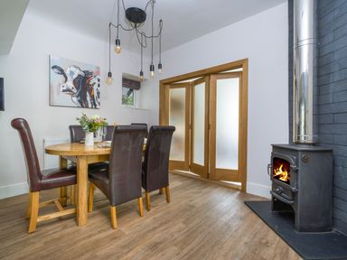 A dining room with a wooden round table and leather chairs and a wood burning stove at Fellside Lodge in Bowness-On-Windermere