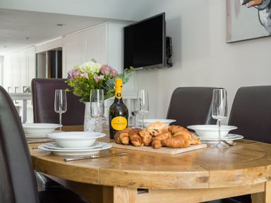 A dining table set with croissants plates glasses bottle of La Gioiosa and flower vase at Fellside Lodge in Bowness-On-Windermere