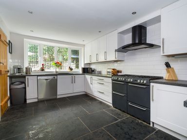 A kitchen with white cabinets black stove dishwasher and large window at Fellside Lodge in Bowness-On-Windermere