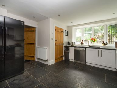 A kitchen with black refrigerator wooden doors white cabinets and a large window with plants outside at Fellside Lodge in Bowness-On-Windermere