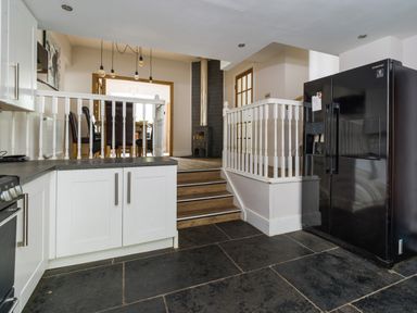 A kitchen area with white cabinets a black refrigerator black stone floor and a dining area with chairs and a wood stove at Fellside Lodge in Bowness-On-Windermere