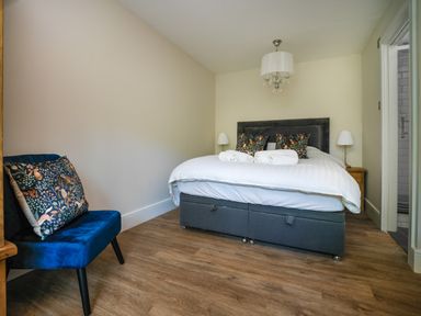A bedroom with a bed and two bedside tables with lamps and a blue chair with a patterned cushion at Fellside Lodge Bowness-On-Windermere