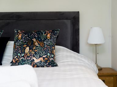A bed with a dark headboard a patterned cushion and a white lamp on a wooden bedside table at Fellside Lodge Bowness-On-Windermere