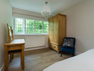 A bedroom with a wooden wardrobe a small wooden desk and a blue chair with a patterned cushion at Fellside Lodge in Bowness-On-Windermere