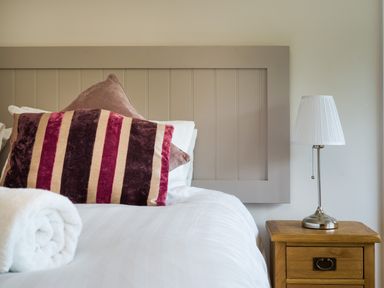 A bed with striped and plain pillows a rolled white towel and a bedside table with a lamp at Fellside Lodge in Bowness-On-Windermere