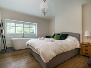 A bedroom with a bed and a freestanding bathtub under a window at Fellside Lodge in Bowness-On-Windermere