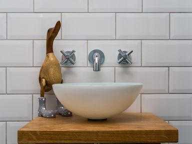 A bathroom sink with a wooden duck figurine wearing gray boots on a wooden counter at Fellside Lodge in Bowness-On-Windermere