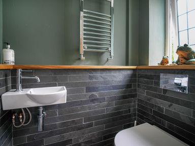 A bathroom with a small sink soap dispenser and toilet with tiled walls and a window at Fellside Lodge in Bowness-On-Windermere