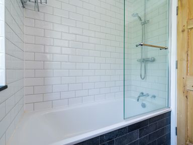 A bathroom with a white bathtub black lower tiles white wall tiles and a showerhead at Fellside Lodge in Bowness-On-Windermere