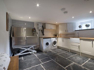 A utility room with washing machines a large stainless steel sink countertop cabinets and a bench at Fellside Lodge in Bowness-On-Windermere